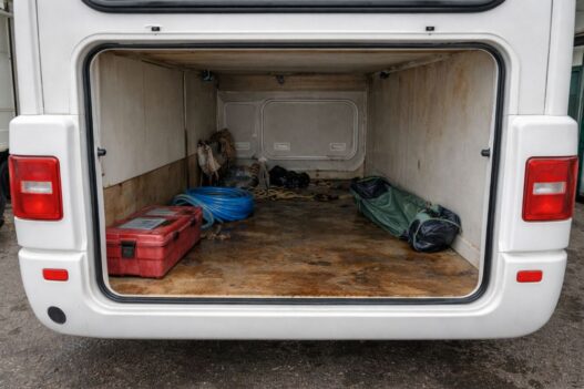 Offener Kofferraum eines Wohnmobils mit Wasserschaden, nasse Gegenstände und sichtbare Schimmel- und Rostspuren an den Wänden und am Boden.